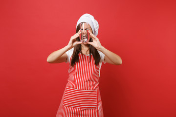 Housewife female chef cook or baker in striped apron white t-shirt toque chefs hat isolated on red wall background. Woman holding drinking clear fresh pure water from glass. Mock up copy space concept