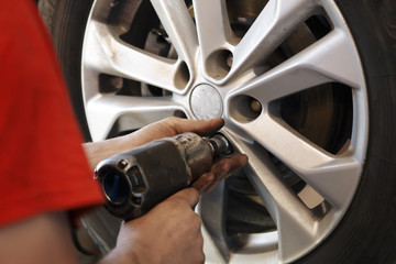 Auto mechanic man with electric screwdriver changing tire outside. Car service. Hands replace tires on wheels. Tire installation concept.