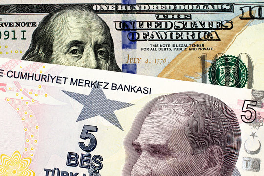 A close up image of a blue American one hundred dollar bill with a five Turkish lira bill