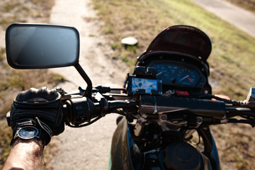 Close-up view on the motorcycle's steering wheel. Hand in leather glove is on the handlebars. Side mirror.