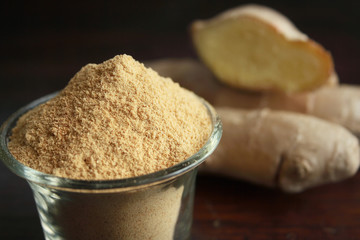 Fresh ginger root and ground ginger spice on wooden background
