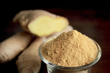 Fresh ginger root and ground ginger spice on wooden background
