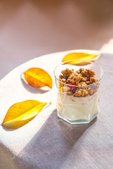 healthy autumn breakfast. Greek yoghurt with granola, dried berries in glass and yellow leaves. Gray background with rustic style tablecloth. Top view copy space lifestyle blogging. Toned image
