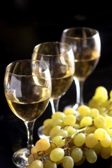 Two glasses of white wine and grape on black background
