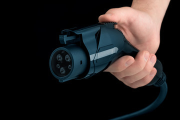 Electric vehicle charging station. Charger for EV car. Man hand holding EV car charger isolated on black background.