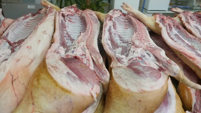 Scary pan shot of fresh swine bodies lying in one line on wooden tables in a spacious butchery. It looks bloody and vicious..