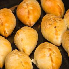 Freshly baked ruddy pies lying on a black steel baking sheet. Close-up view