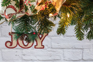 Joy ornament with decorative ribbon on greenery garland against white brick wall