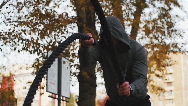Young athlete in Hoodie trains with battle ropes in the autumn park