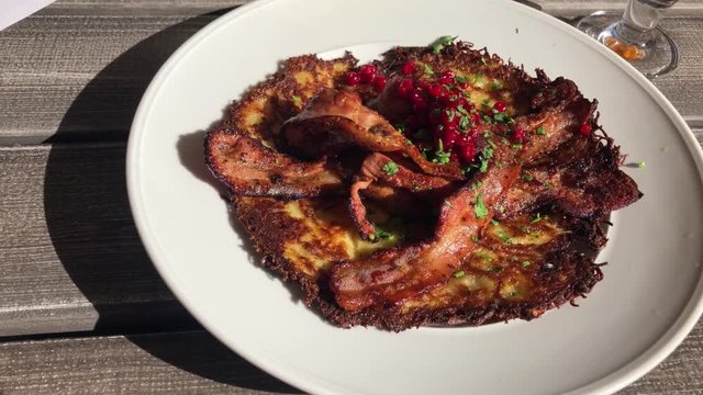 Dolly shot of potato pancake with crispy fried pork and lingonberries served outside a lovely summer eavning.