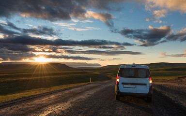 Fototapeta na wymiar Gravel road along the valley at sunset with lonely car. Car travel in Iceland