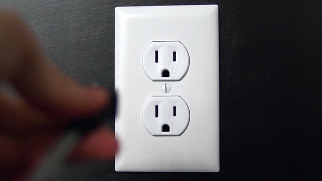 Male hand plugs in and unplugs a two pronged cord into the top outlet of an American electrical socket
