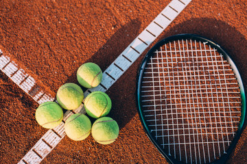 Balls and tennis racket on clay court.