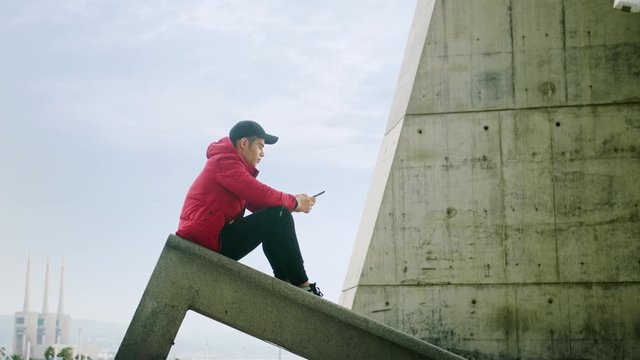 Young Attractive Trendy young Man interacting callling and messaging with a cell phone on an urban city background