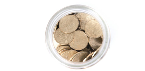 Close up coins in glass jar on white table. Coins scattered around. Isolated on white background