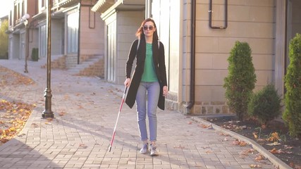 Young blind woman with a backpack with a cane goes through the city sunray,slow mo