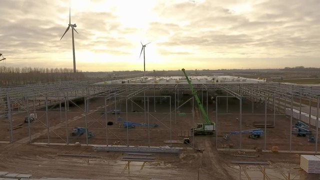 Flying with a drone over a construction site where a warehouse is being build.
