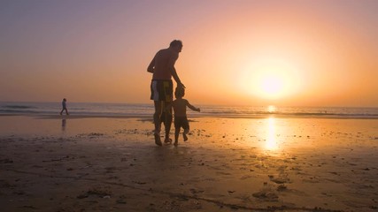 Silhouette of father with two children in the beach at sunset