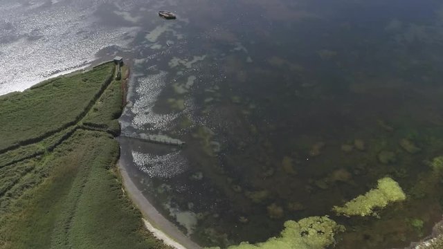Tracking aerial across the fleet lagoon at the Abbotsbury Swannery. A patch of green surface algae has built up. Amazing reflections and detail below the water's surface. Cropped