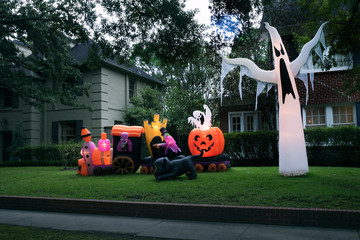 The house is decorated for Halloween: Inflatable train with the dead, big pumpkin, black cat huge and small ghost. Night, Houston, Texas, United States