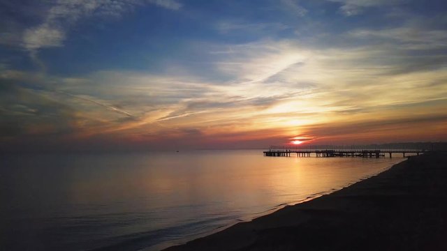 Drone footage of a sunrise over the sea. Slow forward flight on low altitude and rise over the pier. Beautiful colours. Peaceful scenery. Baltic Sea, Gdansk, Poland.