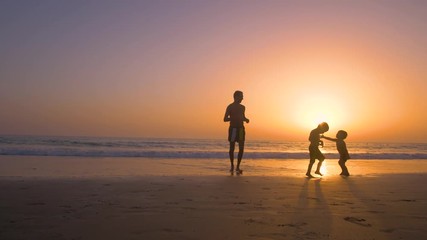 Silhouette of father with two children in the beach at sunset