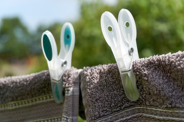 Close-up of two dark towels drying on a clothesline with two large green and yellow clothespins against a blue and green background