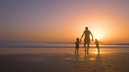 Silhouette of father with two children in the beach at sunset