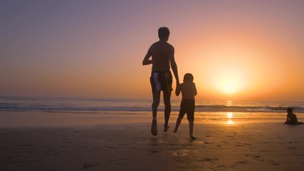 Silhouette of father with two children in the beach at sunset