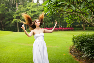 portrait of carefree young woman in white dress posing in green summer park