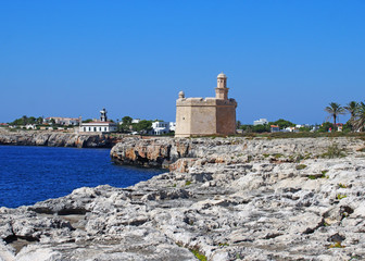 Fototapeta na wymiar a bright sunlit view of the cliffs and coast in ciutadella menorca with deep blue sea and rocky cliffs with the historic castle and lighthouse in the distance