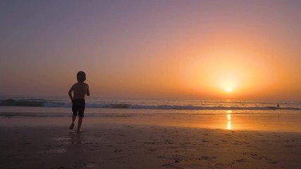 Silhouette of child running and playing  in the beach at sunset - freedom