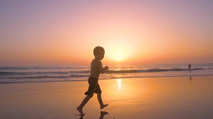Silhouette of child running and playing  in the beach at sunset - freedom