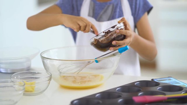 Little girl hands mixing chocolate into yolk to make dough on the bowl in the kitchen at home. Shot in 4k resolution