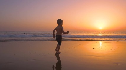 Silhouette of child running and playing  in the beach at sunset - freedom