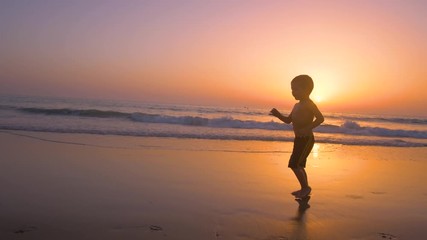 Silhouette of child running and playing  in the beach at sunset - freedom