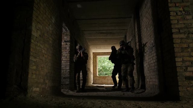 Army soldiers in full uniform during the military operation on enemy territory. Rangers with special equipment, weapons and tactical devices storming the building occupied by enemy during war.