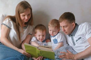 Family mom, dad and two twin brothers read books laying on the bed. Family reading time.