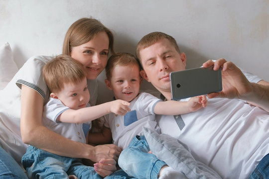 Dad makes family selfie on mobile phone. Mom, dad and two brother twins toddlers.