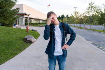 Upset teenager standing on a sidewalk with a high school in the background.