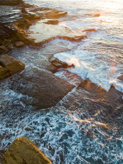 Water flowing at the rocky coastline under the sunrise light.