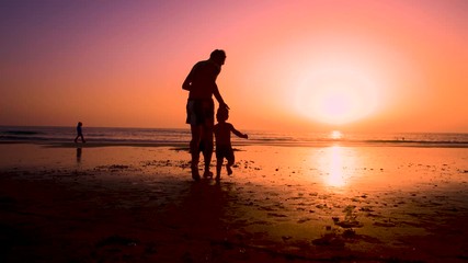 Silhouette of father with two children in the beach at sunset