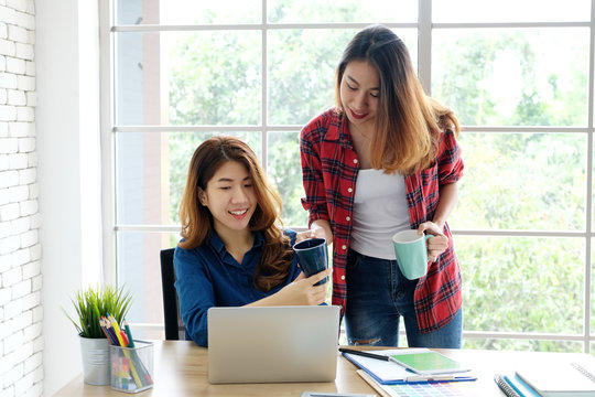 Young asian women holding a coffee cup with smiling face, positive emotion while working with laptop computer, lifestyle, working from home concept