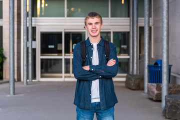 Happy teenager standing in front of the entrance to his high school.