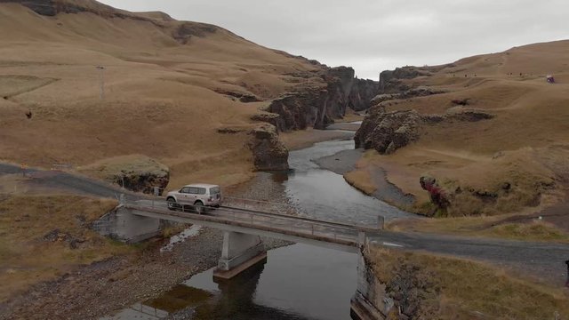 Cinematic aerial flyover of stunning Icelandic canyon with 4x4 crossing the bridge in front.