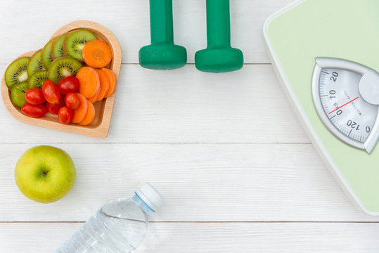 Diet and weight loss for healthy care with  weight scale and fitness equipment,fresh water and fruit healthy, green apple, banana, carrot on white wooden background top view.  Healthy Concept..