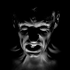 Stylish portrait of adult caucasian man with very angry face and who seems like maniac or devil. Black and white shot, low-key lighting.