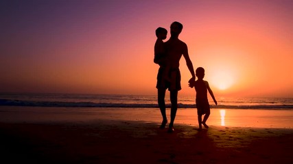 Silhouette of father with two children in the beach at sunset