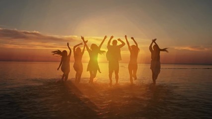 Big crowd of friends having fun at sunset sea beach. Beach vacations concept. Beauty and joyful teenager friends having fun, dancing, spraying over summer sunset. Beach party. Sun flare. Slow motion - Powered by Adobe
