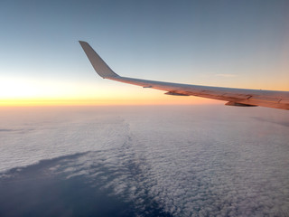 Obraz premium Sunrise Casting Orange tones onto Left Wing of Airplane at High Altitude